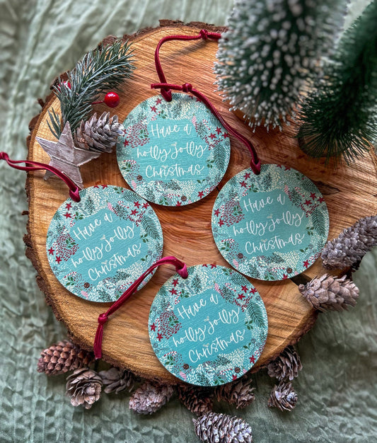 Set of 4 Wooden hanging decorations with 'Have a holly jolly Christmas' on it and a deep red velvet ribbon on a wooden slice with pinecones and a small tree.