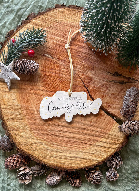 Wooden hanging decoration with 'Wonderful Counsellor' on it and a creamy gold velvet ribbon on a wooden slice with pinecones and a small tree.