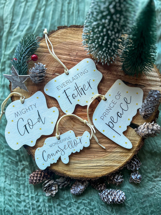 Wooden hanging decorations with 'Wonderful Counsellor', 'Everlasting Father', 'Mighty God' and 'Prince of Peace' on it and a creamy gold velvet ribbon on a wooden slice with pinecones and a small tree.