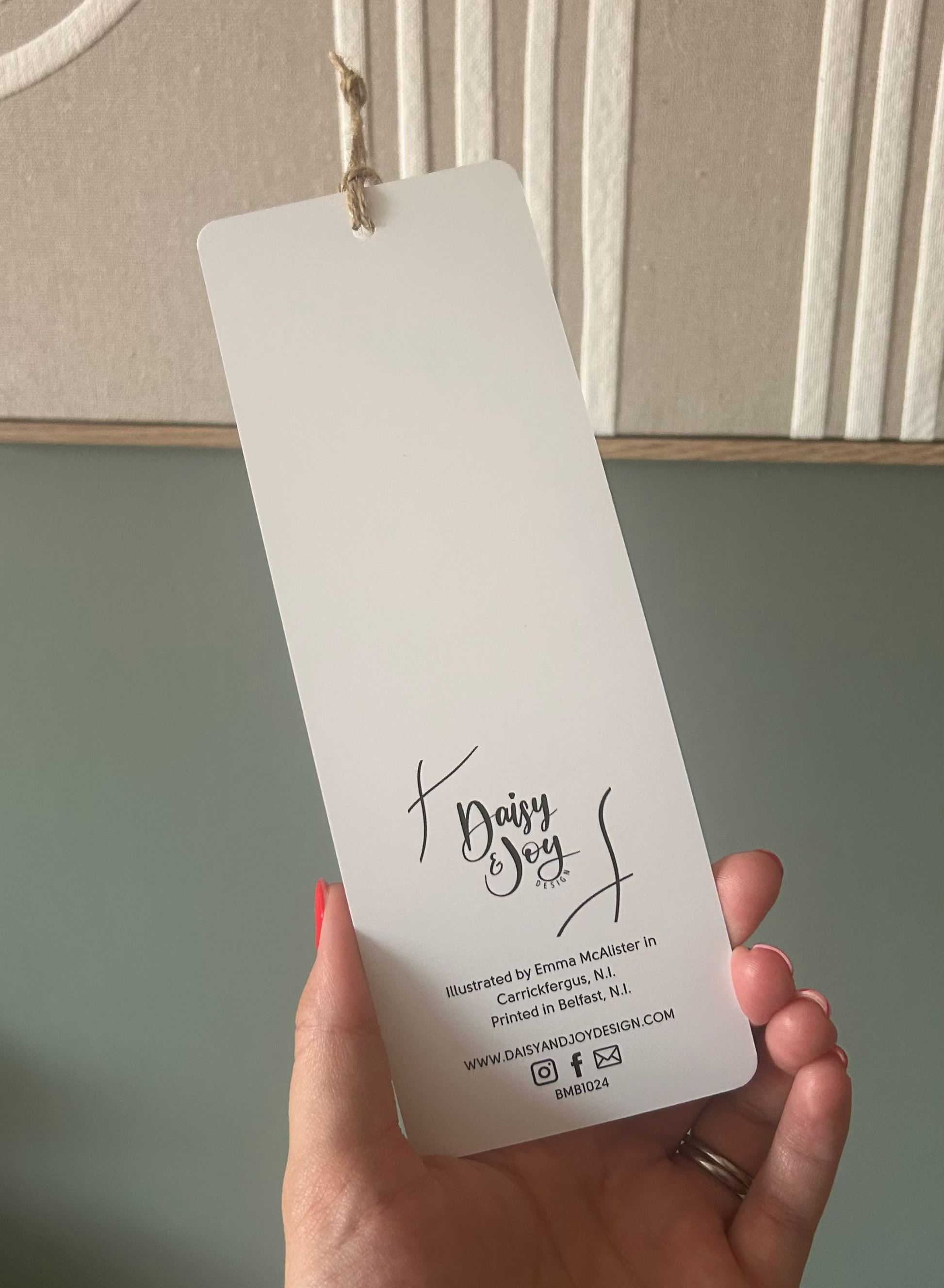A hand holding a blank white paper bookmark or tag with the brand name 'Dairy Soul' printed on it, set against a styled home background with a textured wall and framed art.