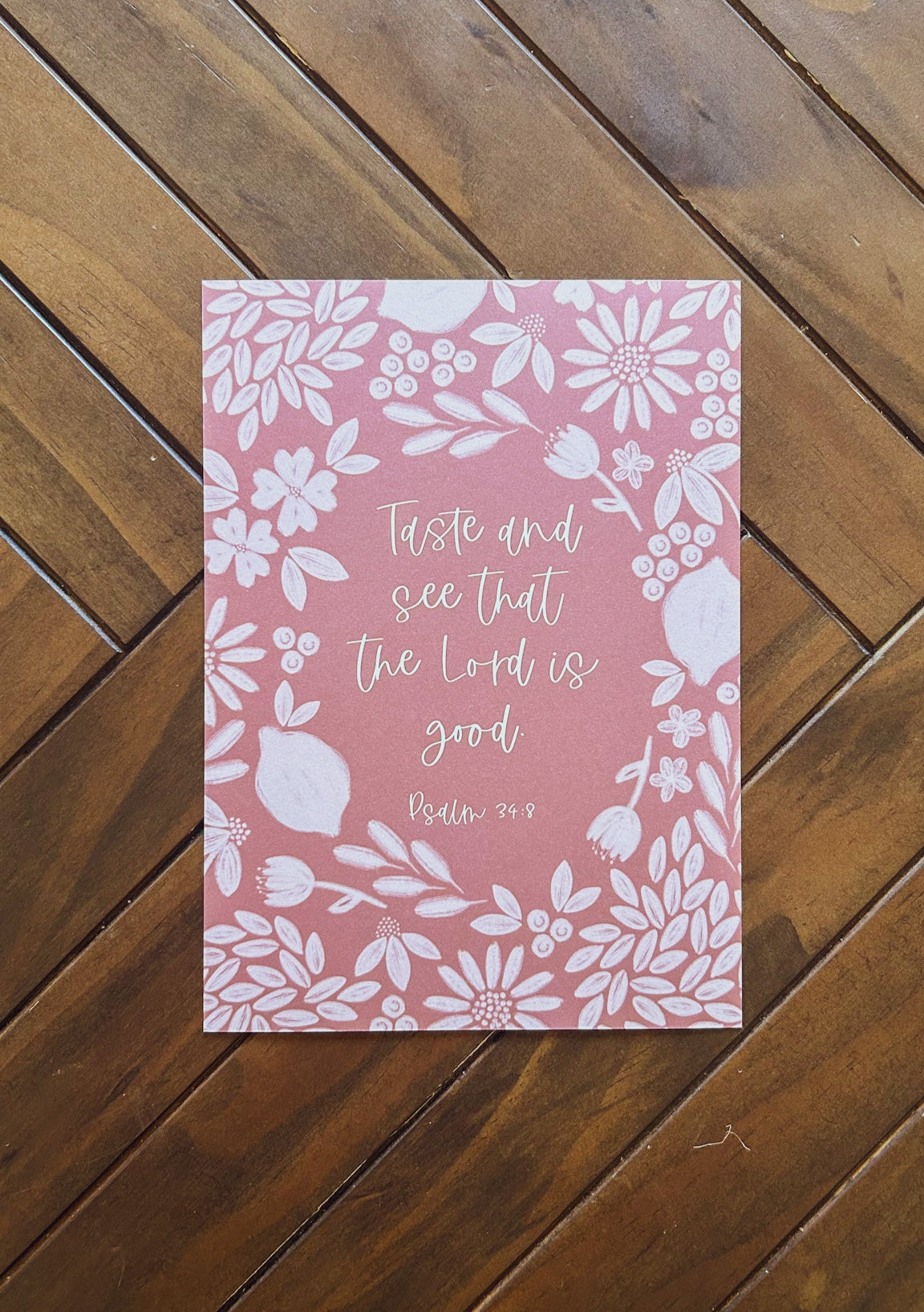 Pink bible verse print with floral design and text on a wooden surface