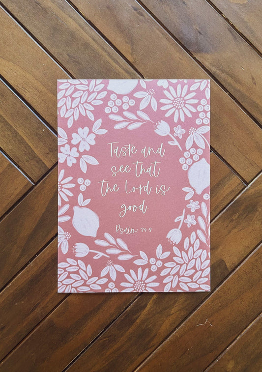 Pink bible verse print with floral design and text on a wooden surface