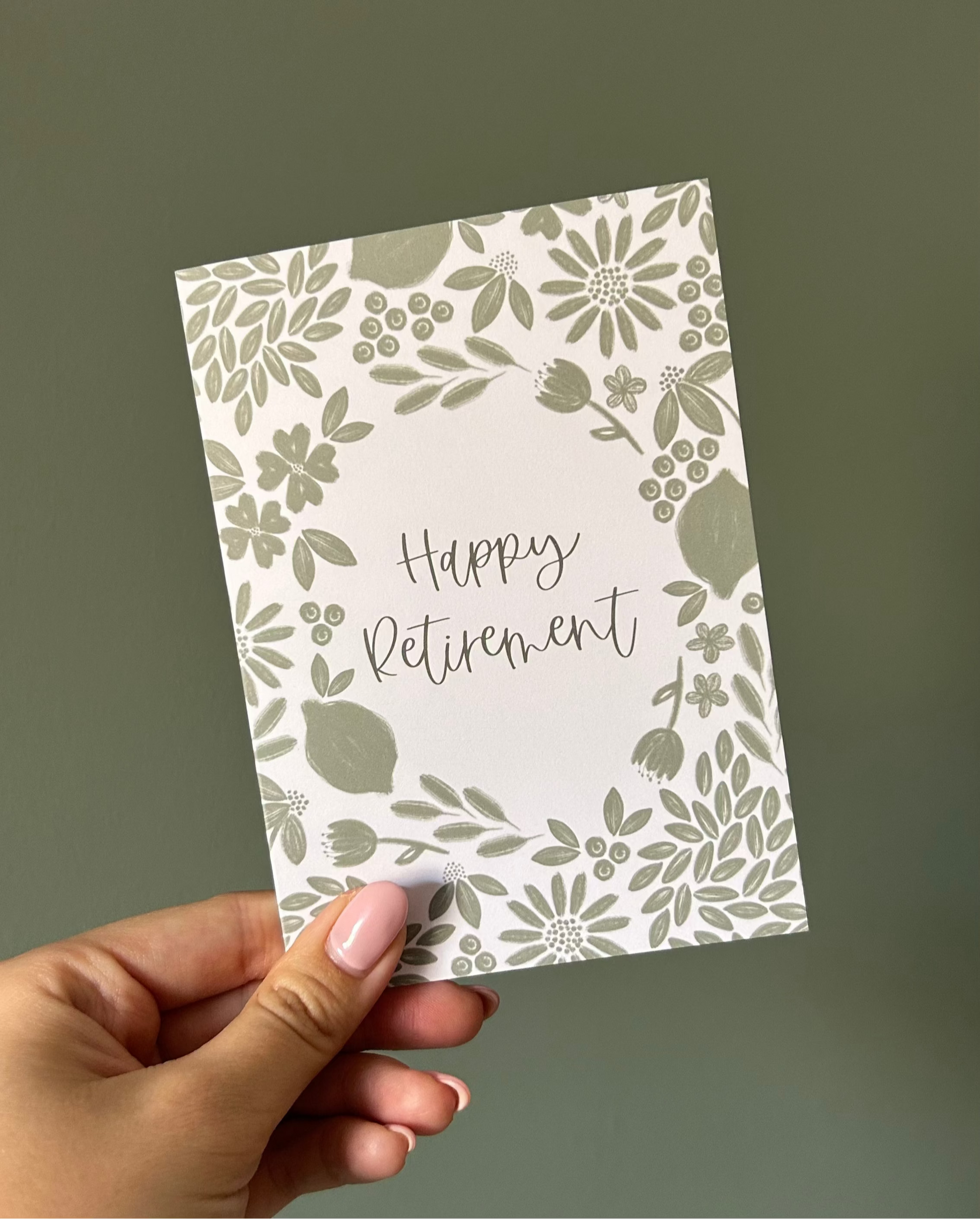 Hand holding a 'Happy Retirement' card with green floral design on a plain background