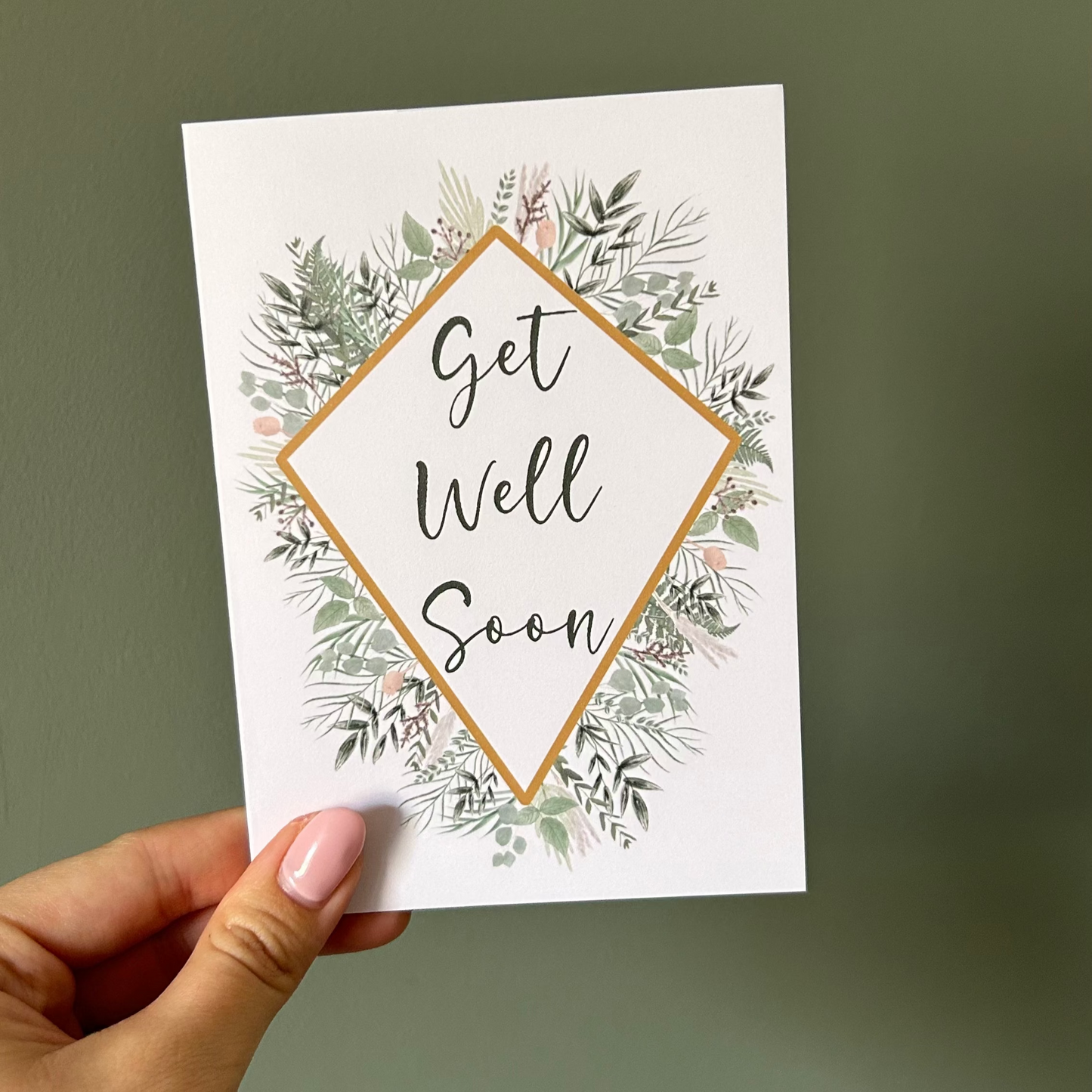 Hand holding a 'Get Well Soon' card with floral design against a plain background