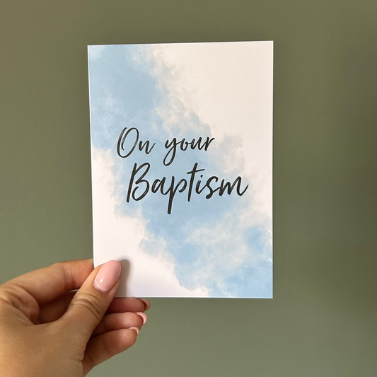 Hand holding a card with 'On your Baptism' text against a plain background