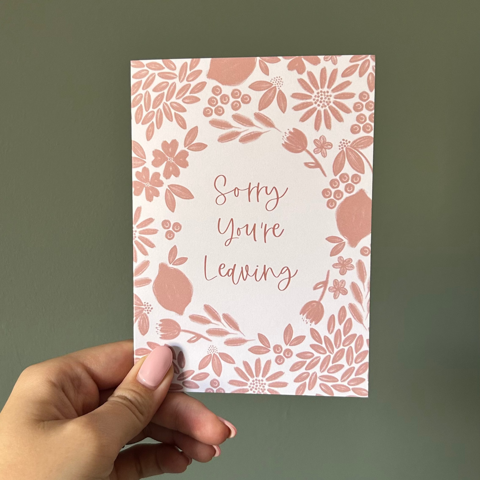 Hand holding a card with floral design and Sorry you're leaving on a plain background