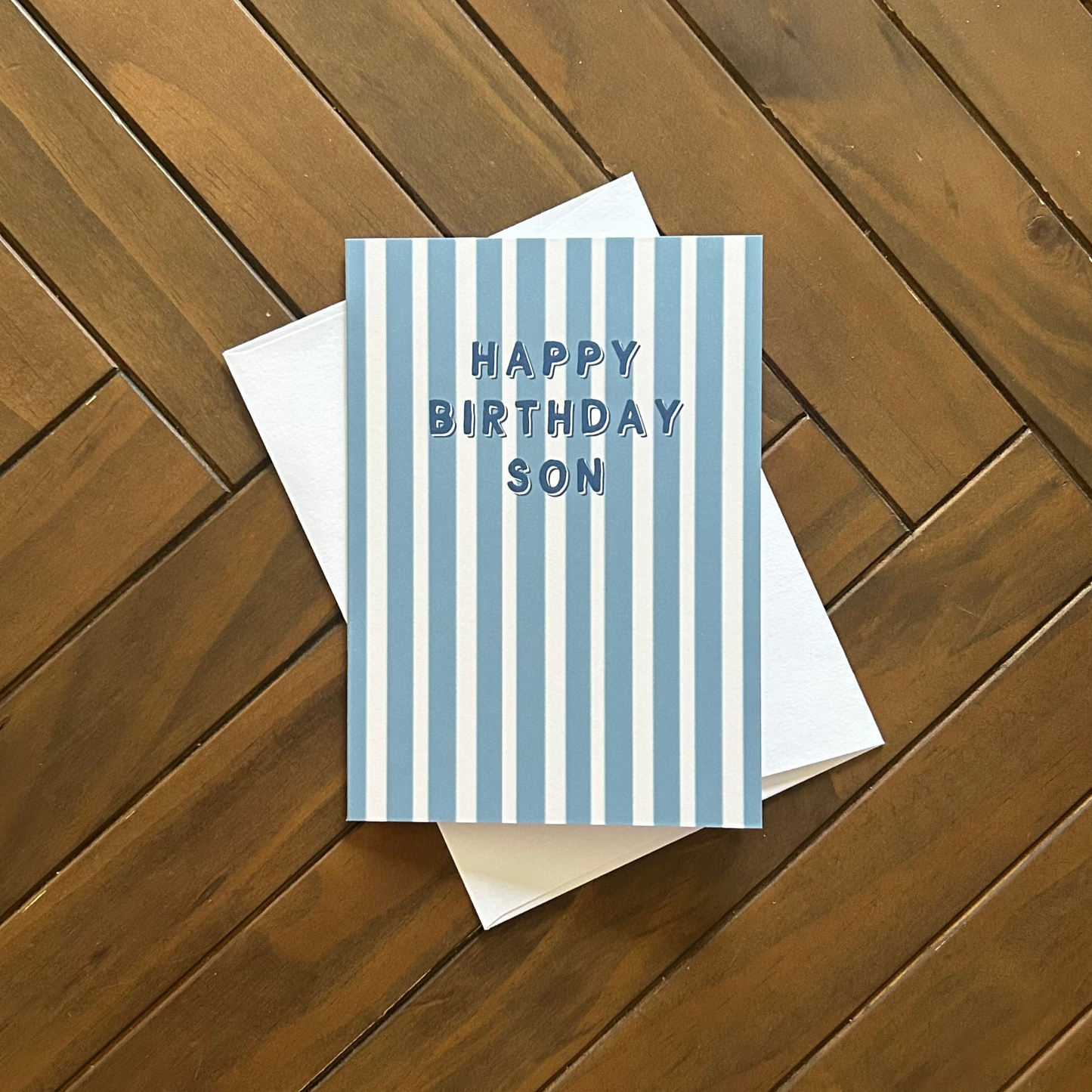 Greeting card with blue stripes and 'Happy Birthday Son' text on a wooden surface