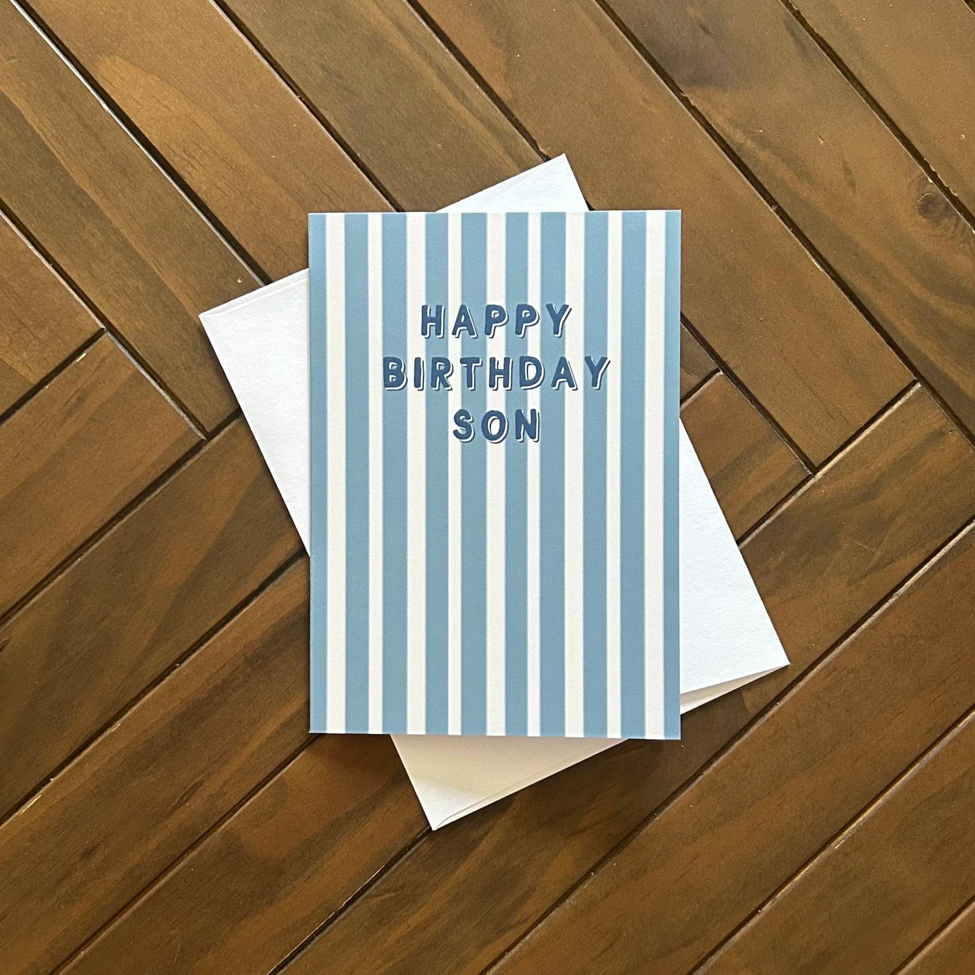 Greeting card with blue stripes and 'Happy Birthday Son' text on a wooden surface