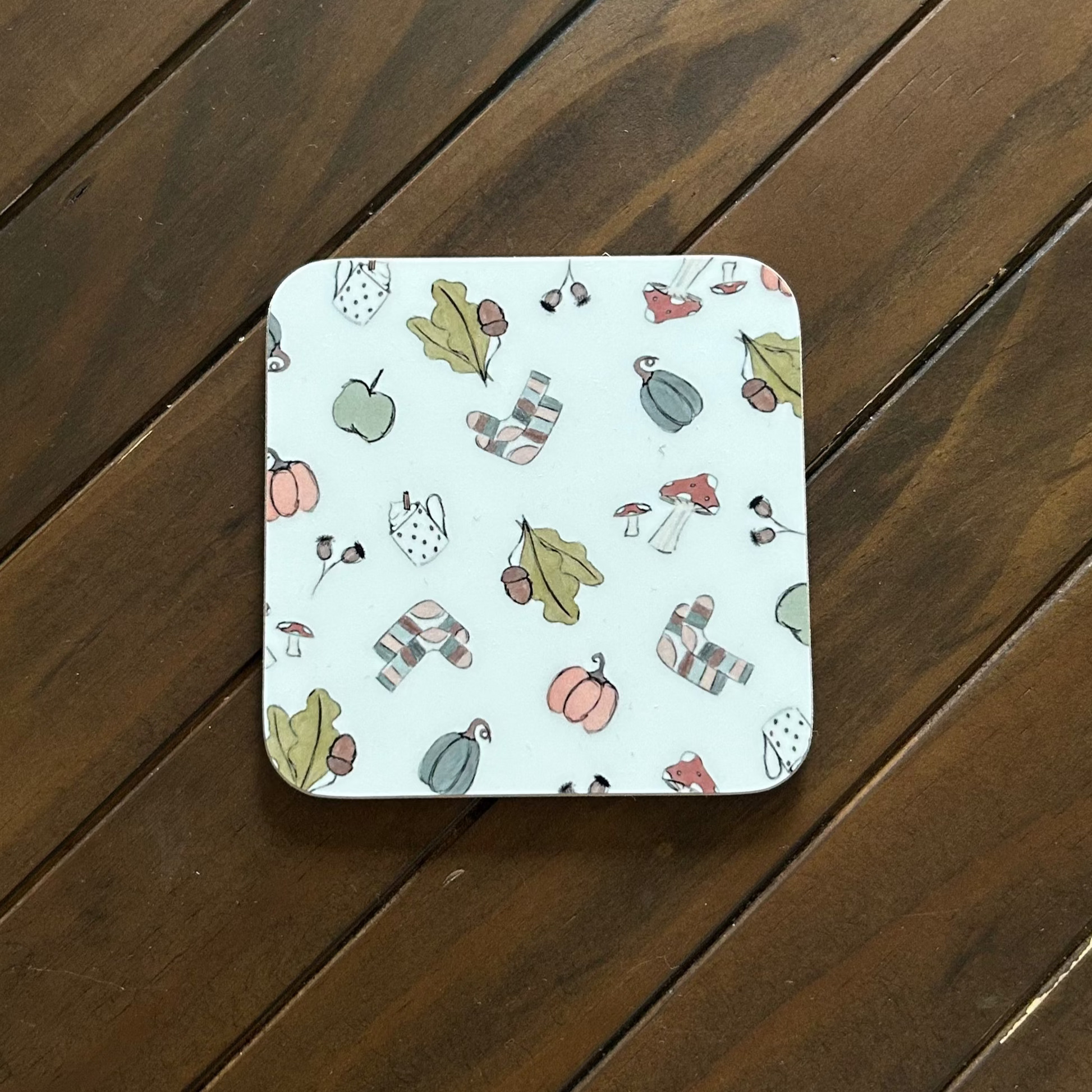 Square coaster with cosy autumnal sketches pattern on a wooden surface
