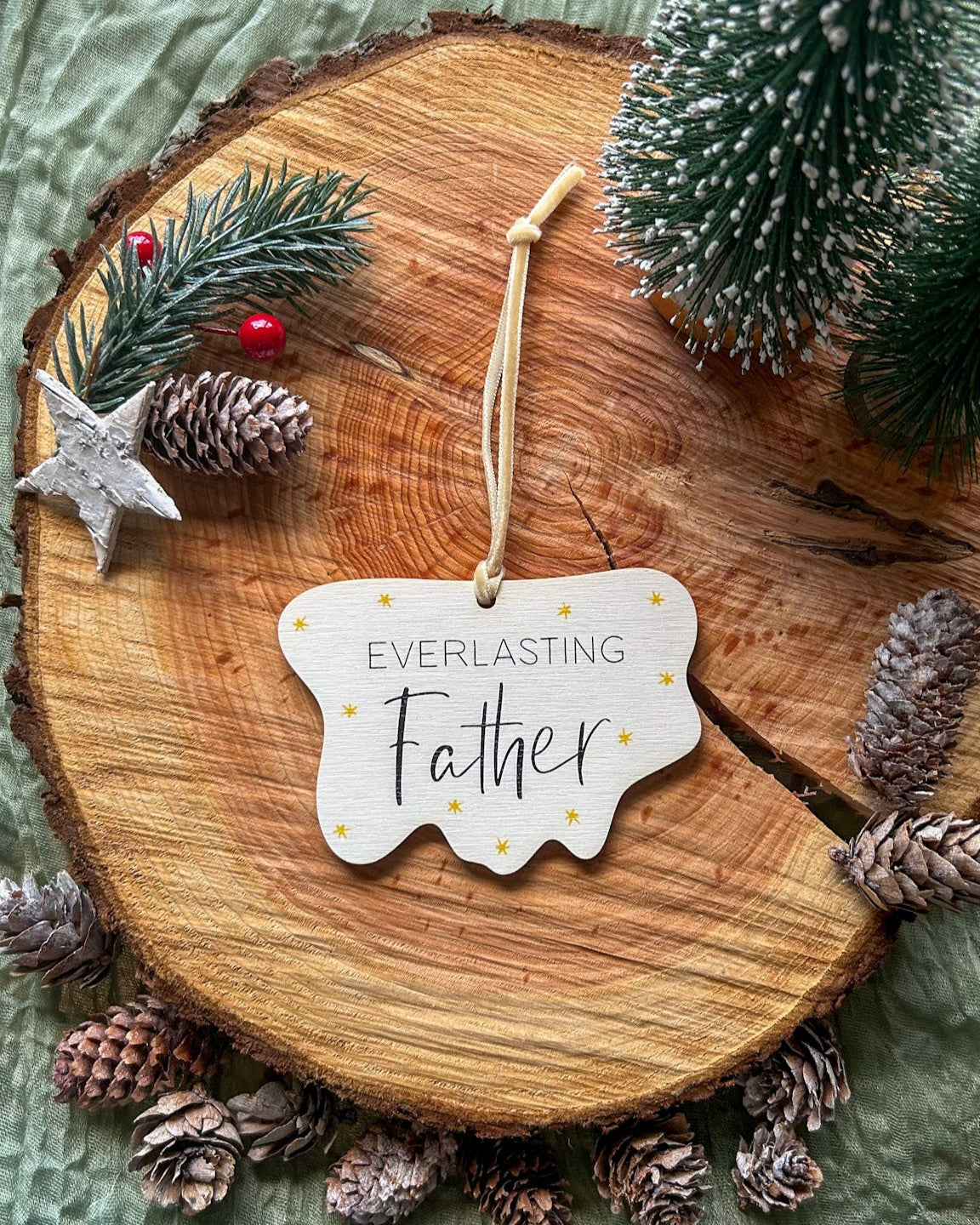 Wooden hanging decoration with 'Everlasting Father' on it and a creamy gold velvet ribbon on a wooden slice with pinecones and a small tree.